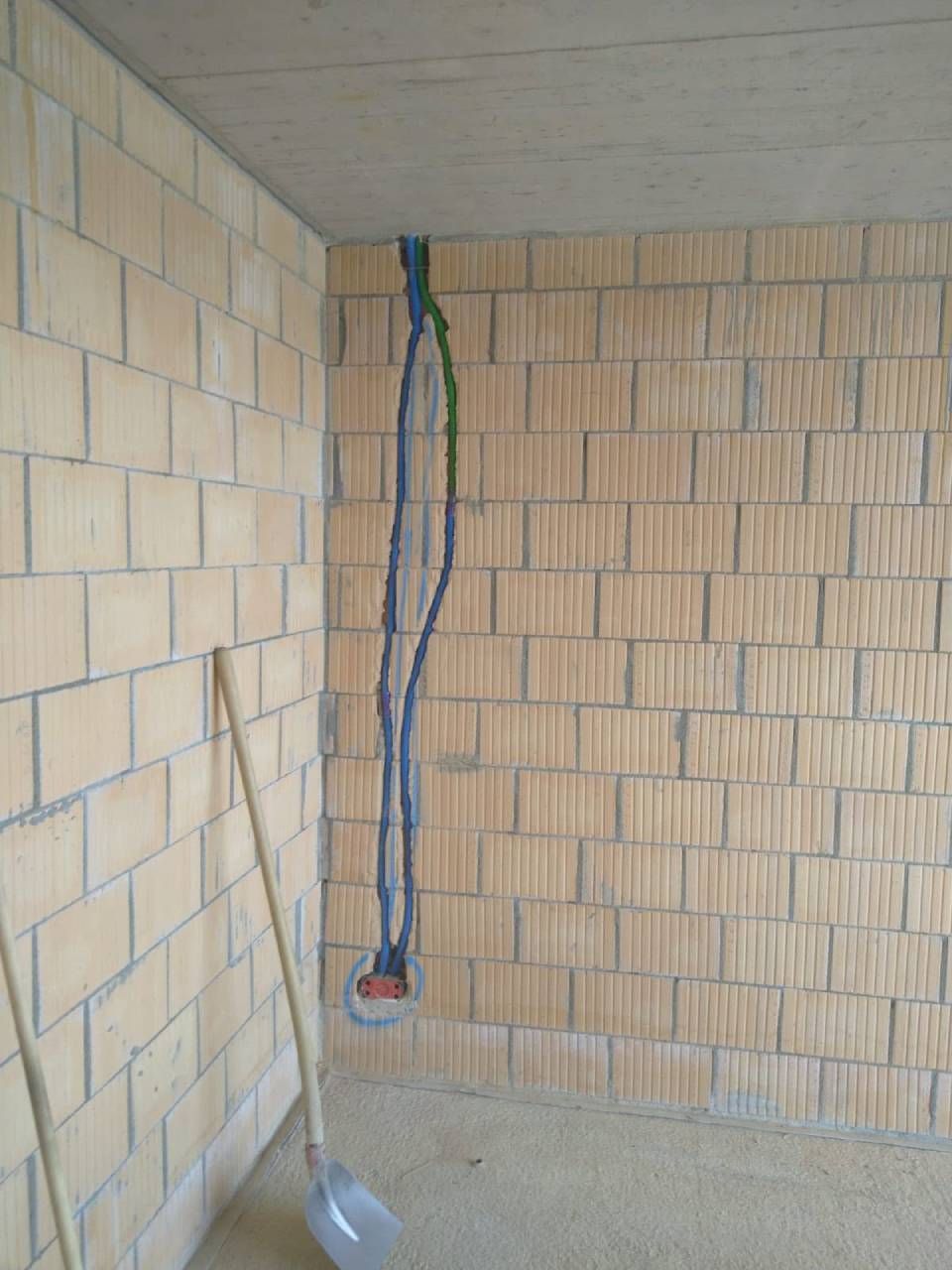 Ein kahler Raum mit unverputzten Ziegelwänden und freiliegenden elektrischen Leitungen, die aus der Ecke hängen.