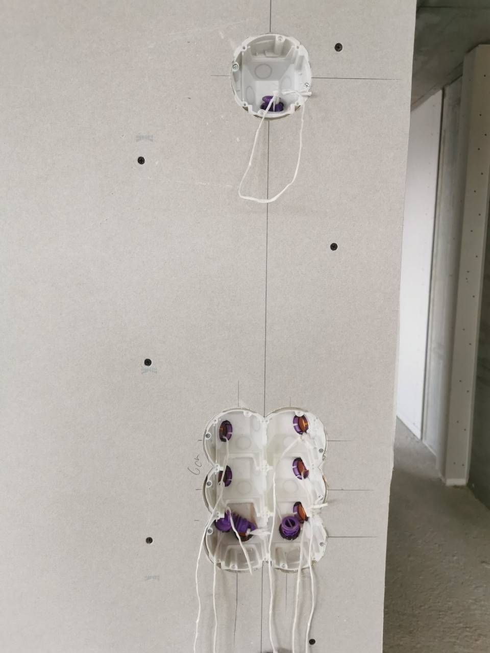 Weisse Wand mit einer hängenden weissen Schnurornament, die mit kleinen lila und braunen Punkten verziert ist.