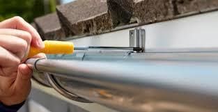 Persona que utiliza un destornillador para instalar un soporte de canalón en una casa.