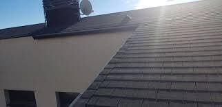 Un techo de tejas oscuras, una pared color crema y una chimenea. La luz del sol brilla desde lo alto.