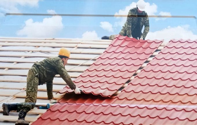 Dos trabajadores instalando tejas metálicas rojas en una casa bajo un cielo azul.