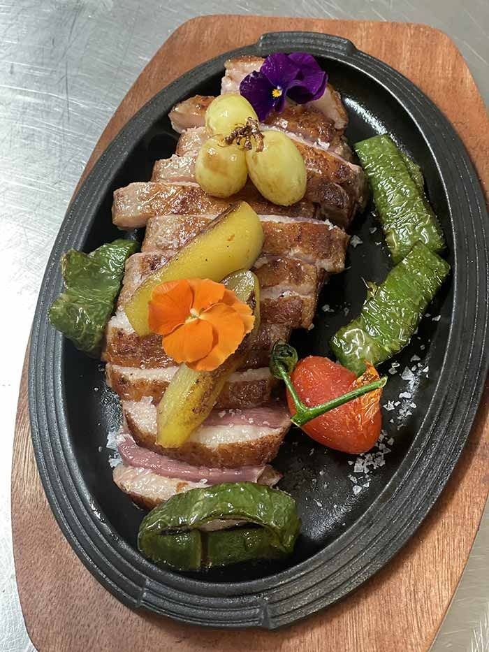 Un plato de comida con carne y verduras en una tabla de cortar de madera.