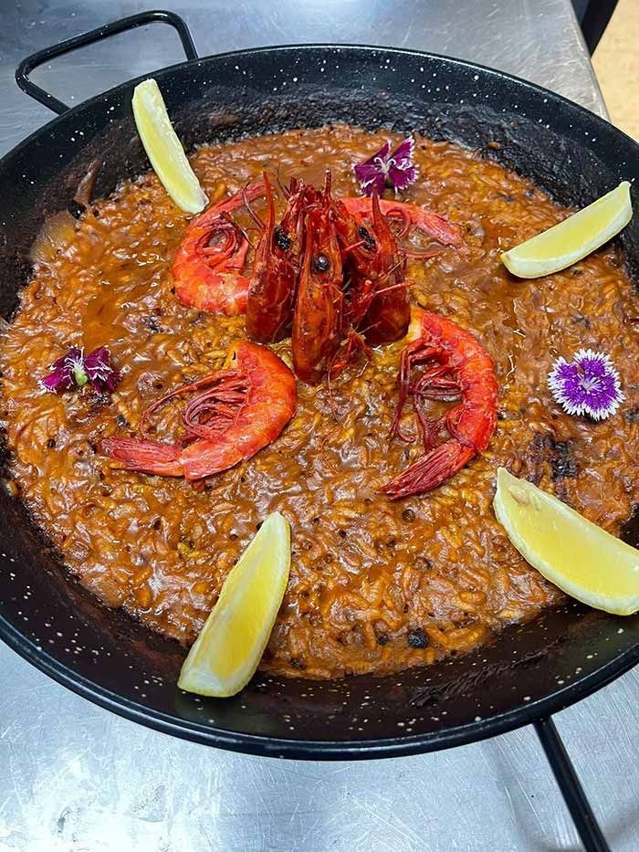 Una sartén de comida con camarones y rodajas de limón encima.