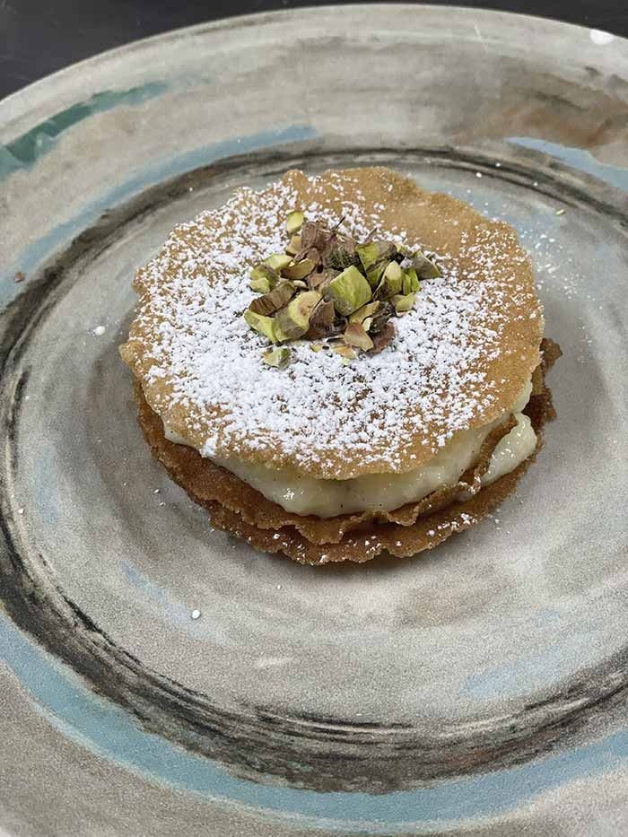 Un primer plano de un postre en un plato con azúcar en polvo y pistachos.