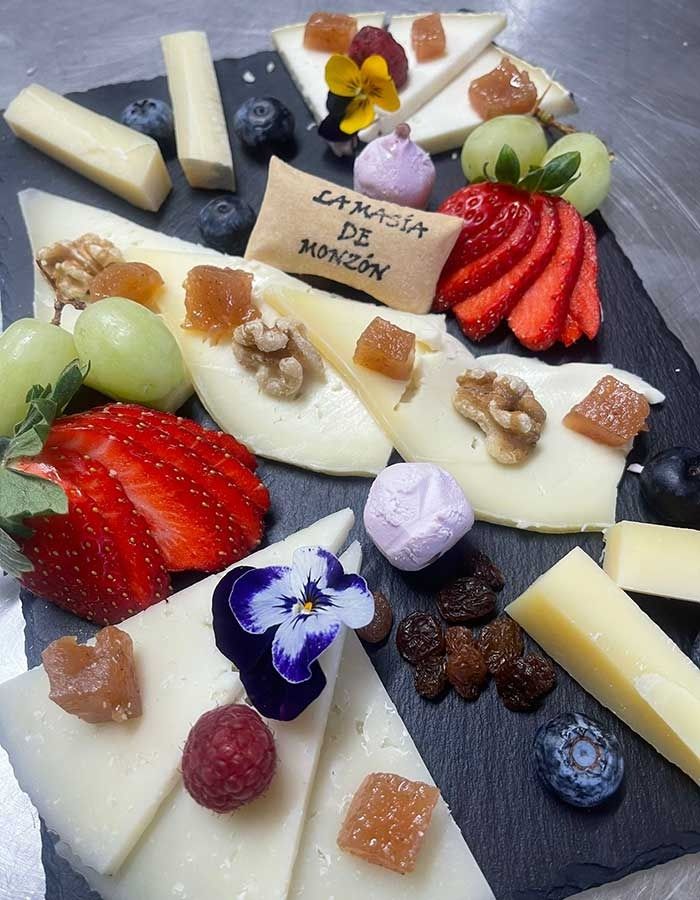 Una variedad de quesos y frutas en un plato negro.