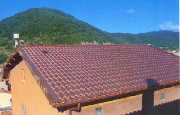 Una casa con techo de tejas rojas y montañas al fondo.