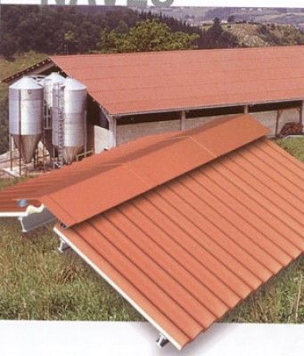 Un granero con techo rojo y silos al fondo.