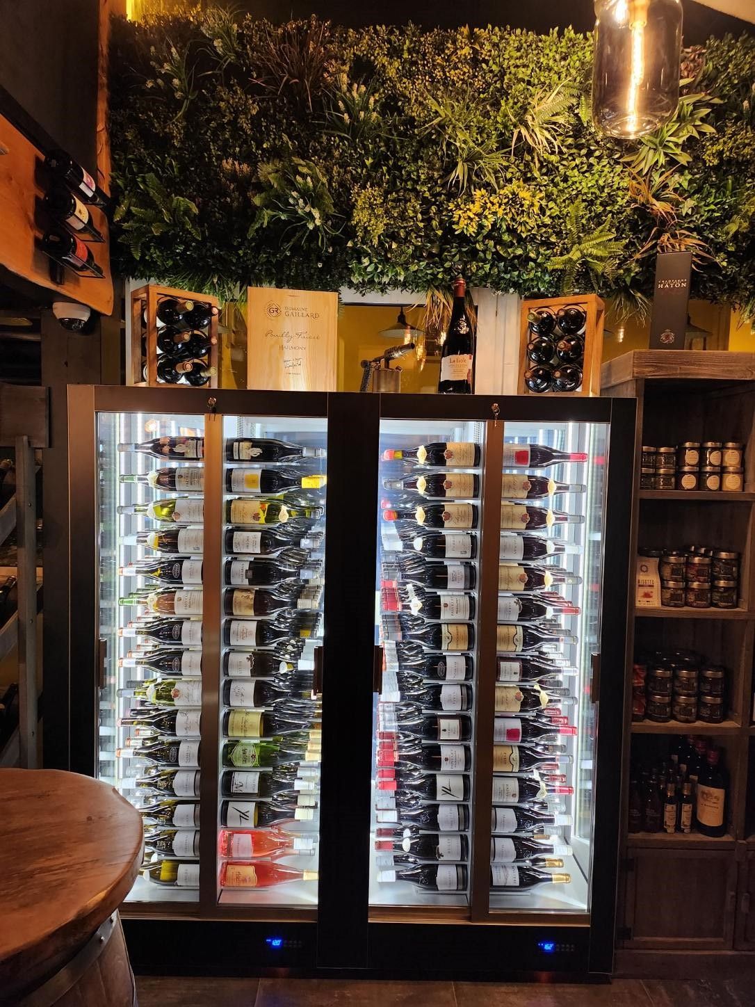 Cave à vin adossé à un mur vert contenant des bouteilles. Photo d'intérieur avec des étiquettes et un éclairage visibles.