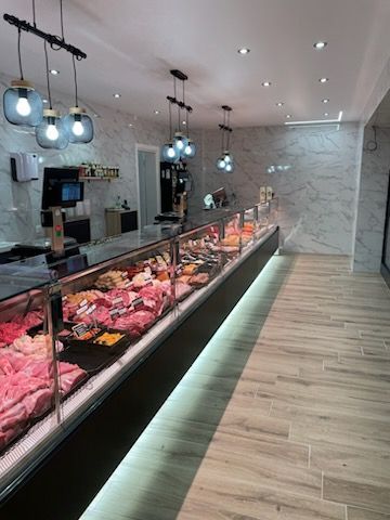 Boucherie avec une longue vitrine remplie de viande, un éclairage moderne et un sol imitation bois.