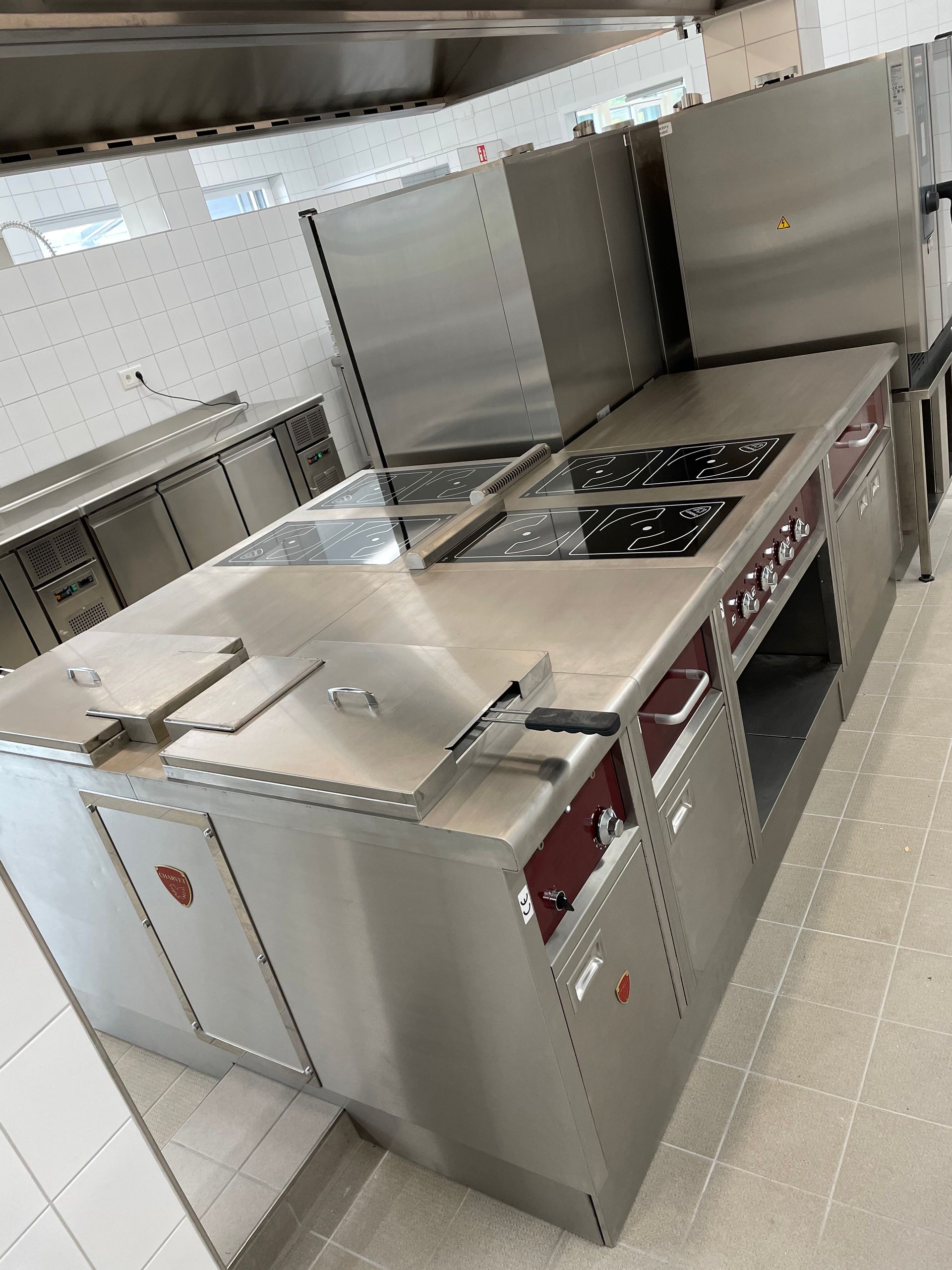 Îlot de cuisine professionnel en acier inoxydable avec des plaques de cuisson, des fours et des rangements.
