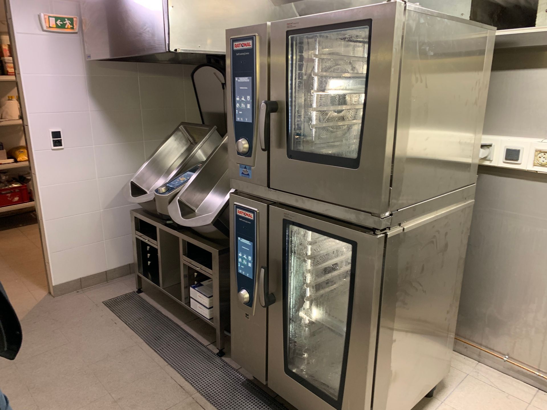 Équipement de cuisine professionnelle : Deux fours superposés, deux poêles basculantes et une hotte aspirante.