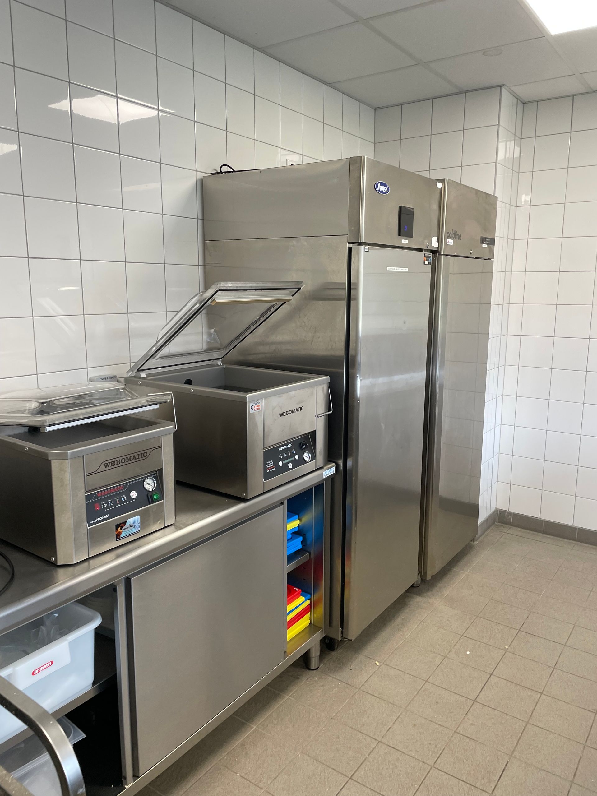 Équipements de cuisine professionnels en acier inoxydable contre un mur carrelé blanc.