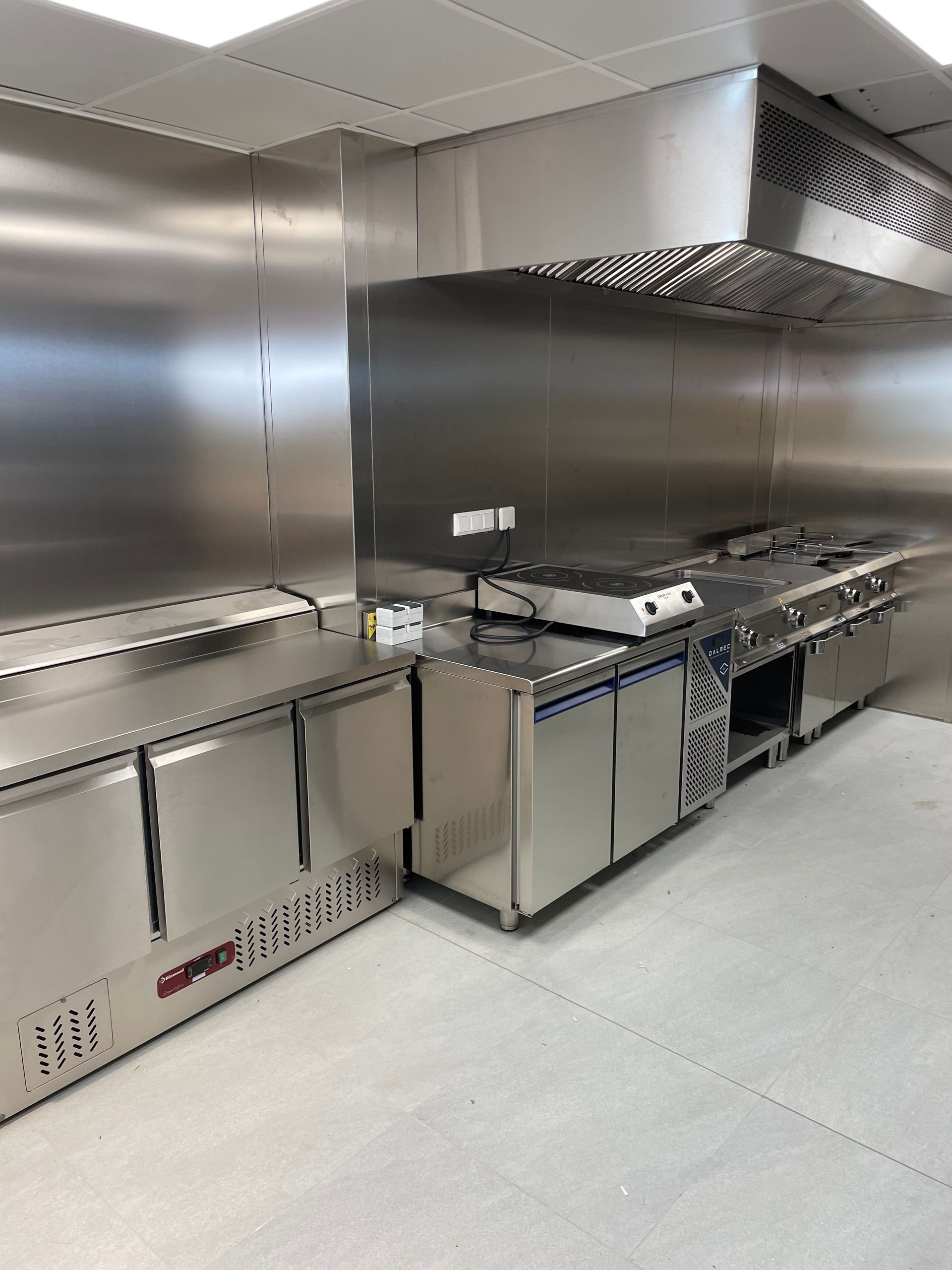 Cuisine commerciale en acier inoxydable avec des appareils électroménagers et une hotte aspirante.