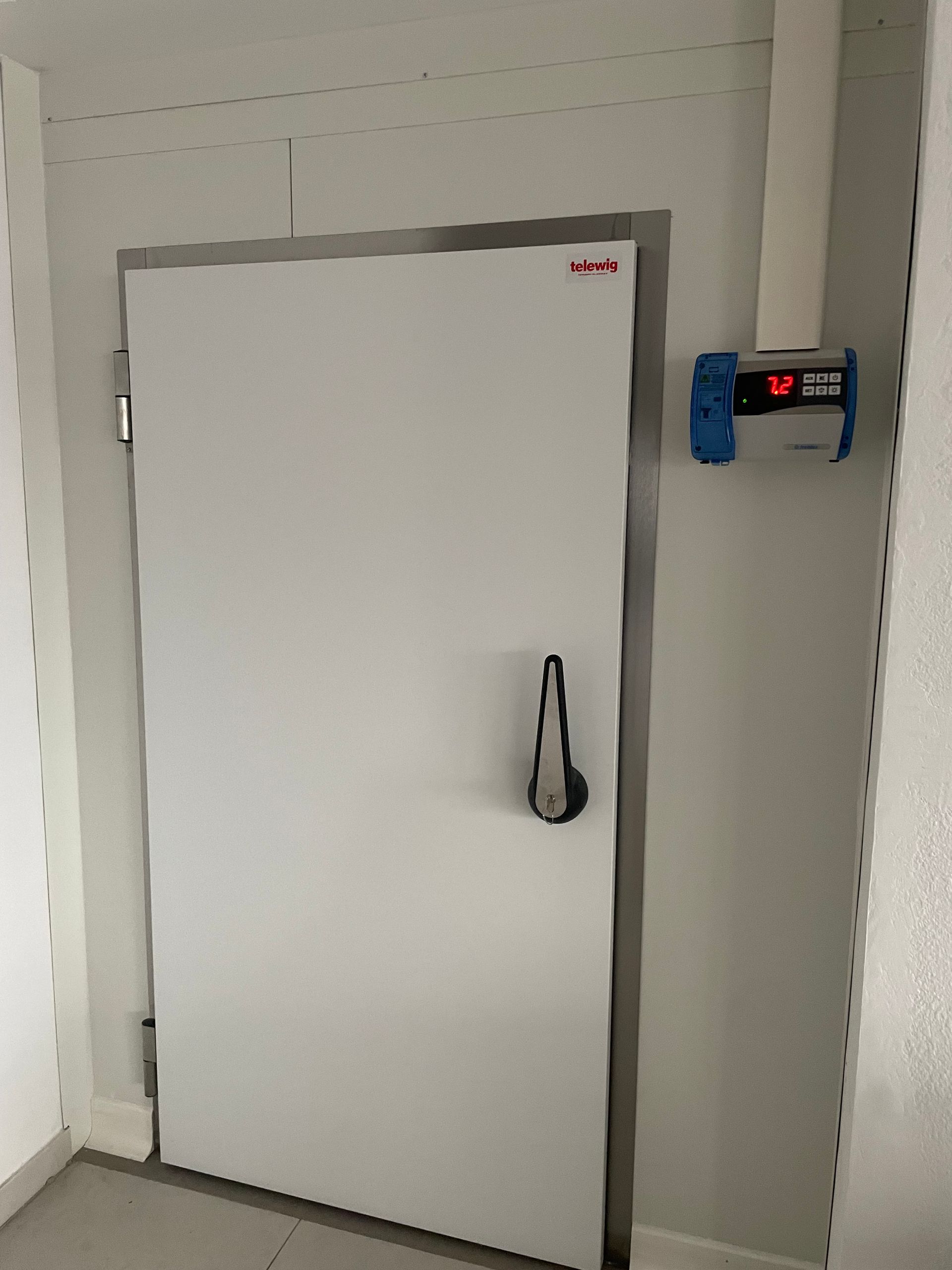 Une porte de chambre froide blanche avec une poignée et un thermomètre mural.