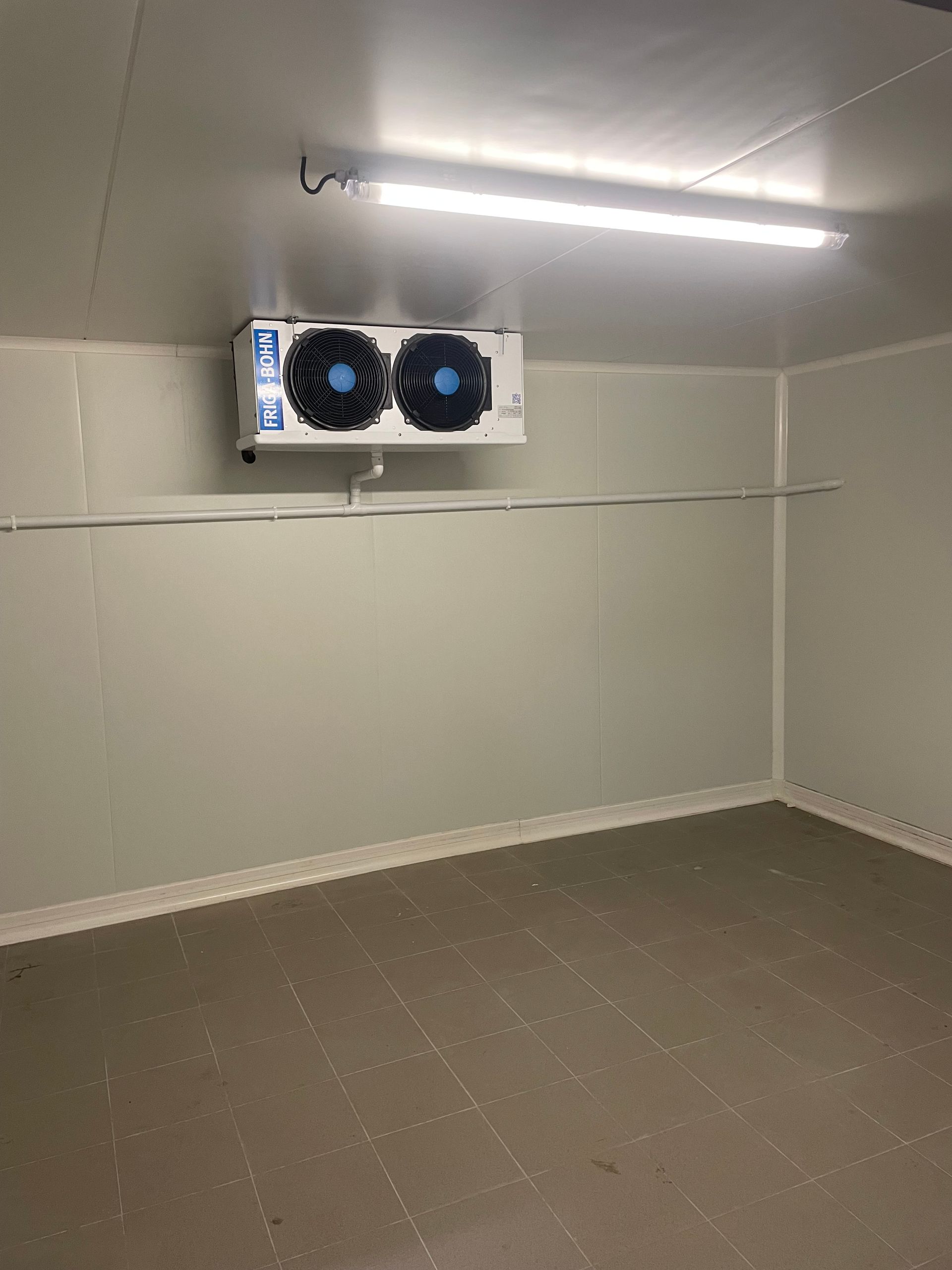 Chambre froide vide avec un groupe frigorifique, un éclairage fluorescent, des murs et un sol gris.