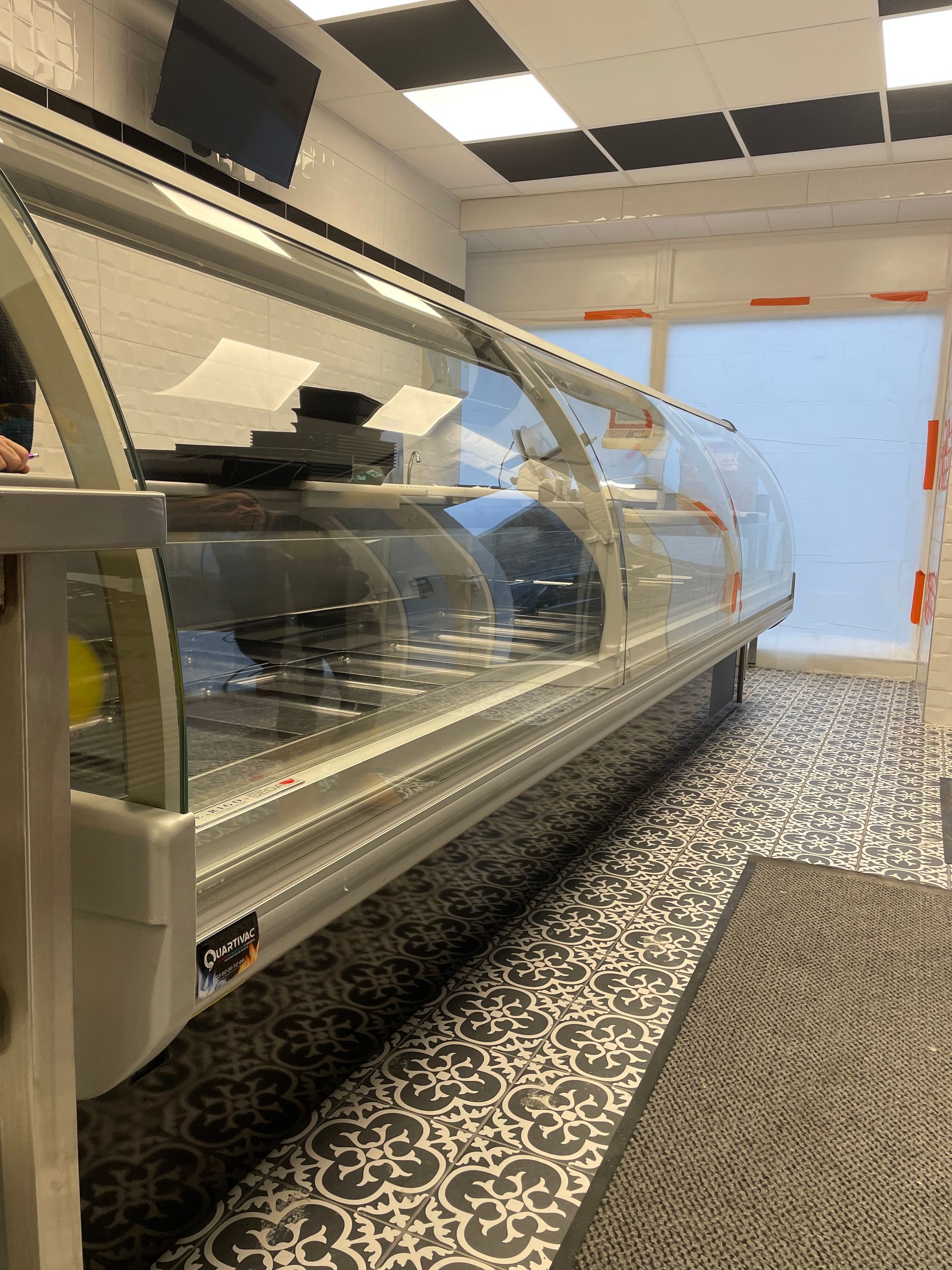 Vitrine alimentaire dans un magasin, à côté d'une porte. Sol à motifs gris et noirs.