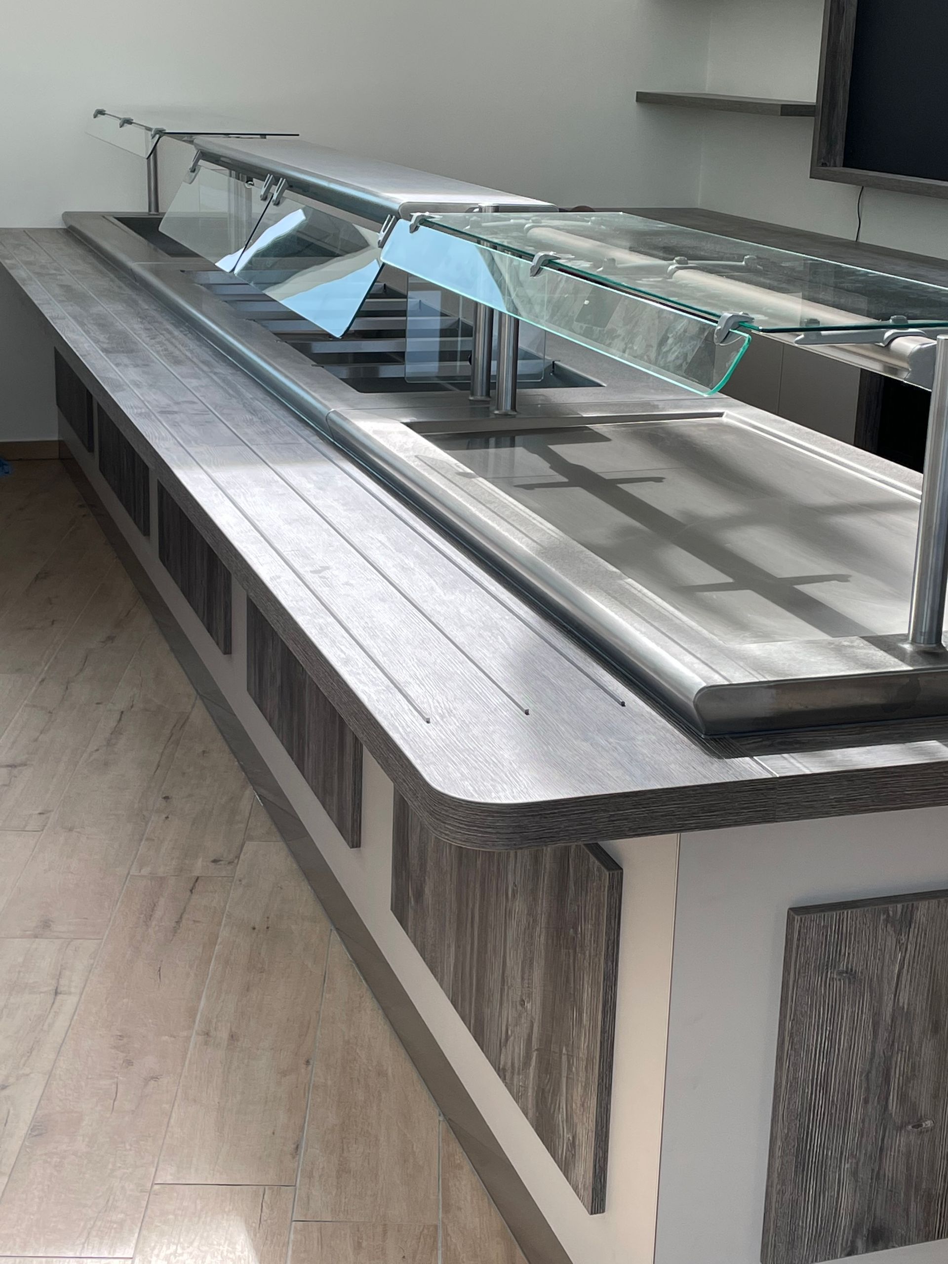 Longue table de buffet avec un plateau gris et une vitre de protection contre les éternuements.