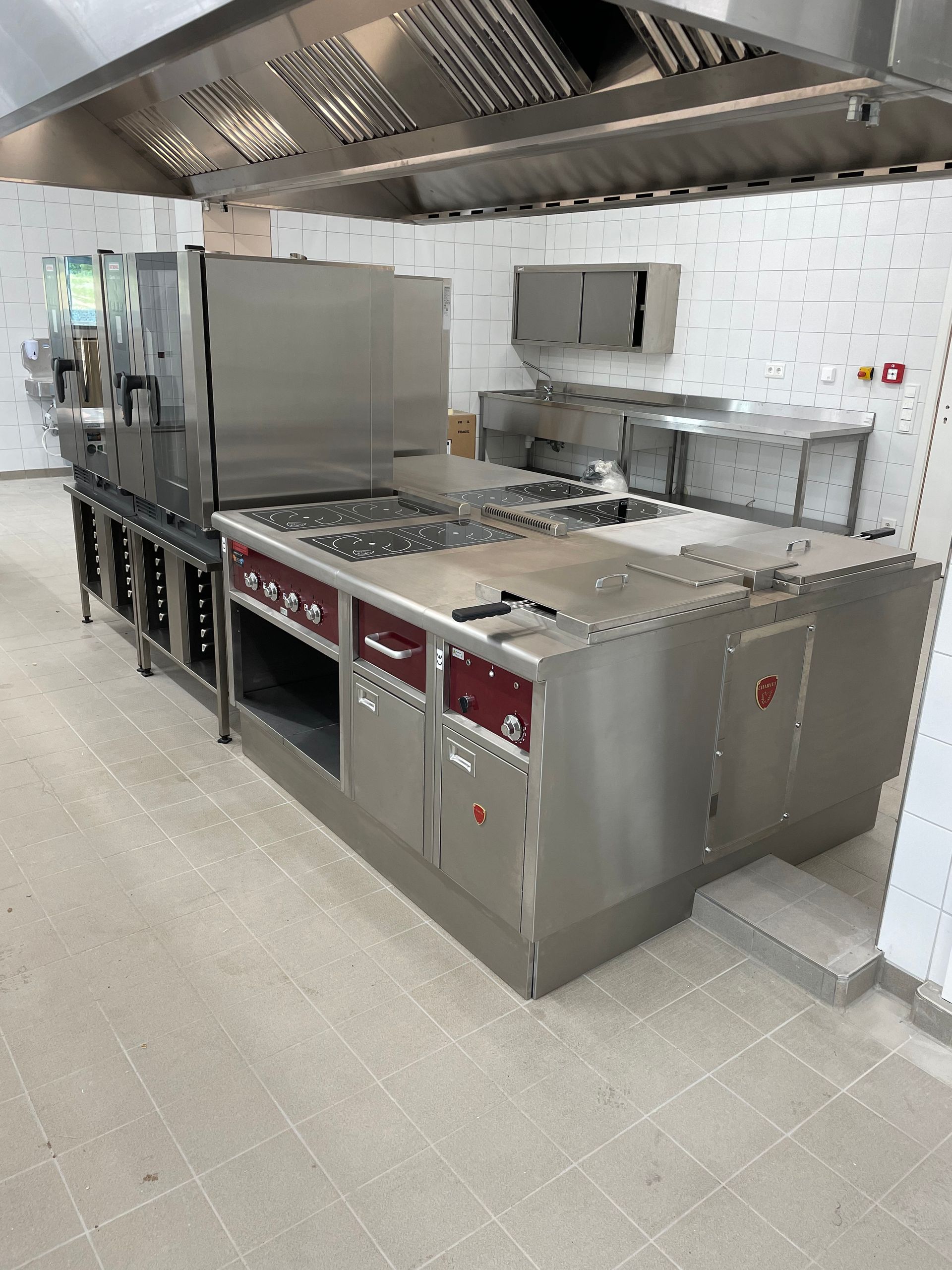 Cuisine commerciale en acier inoxydable avec des surfaces de cuisson, un four et une hotte aspirante.