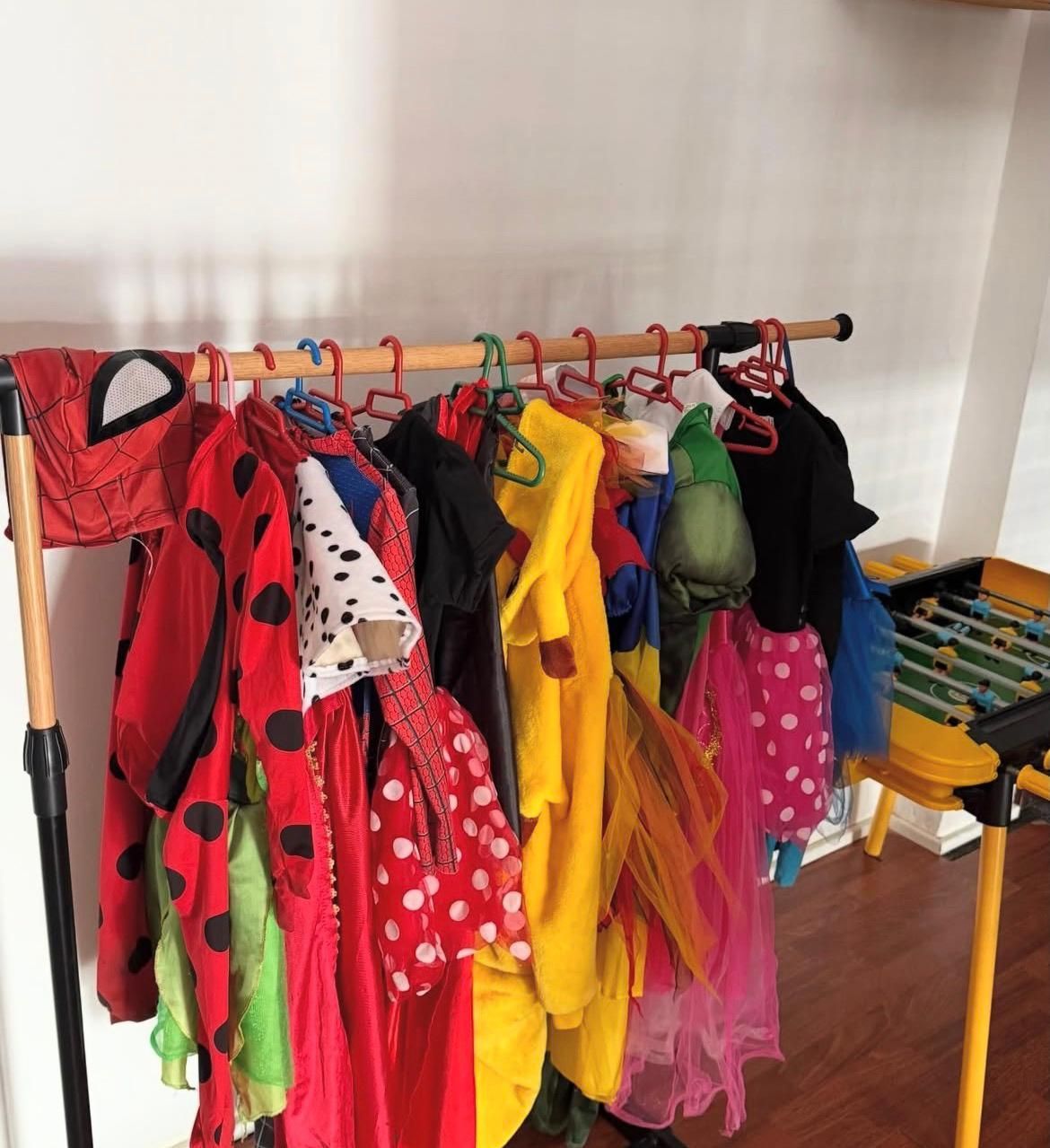 Un perchero con disfraces de Halloween variados para niños, colgados en perchas de plástico contra una pared blanca.