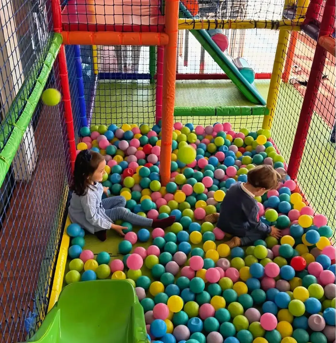 Dos niños juegan en una colorida piscina de bolas dentro de un parque infantil 