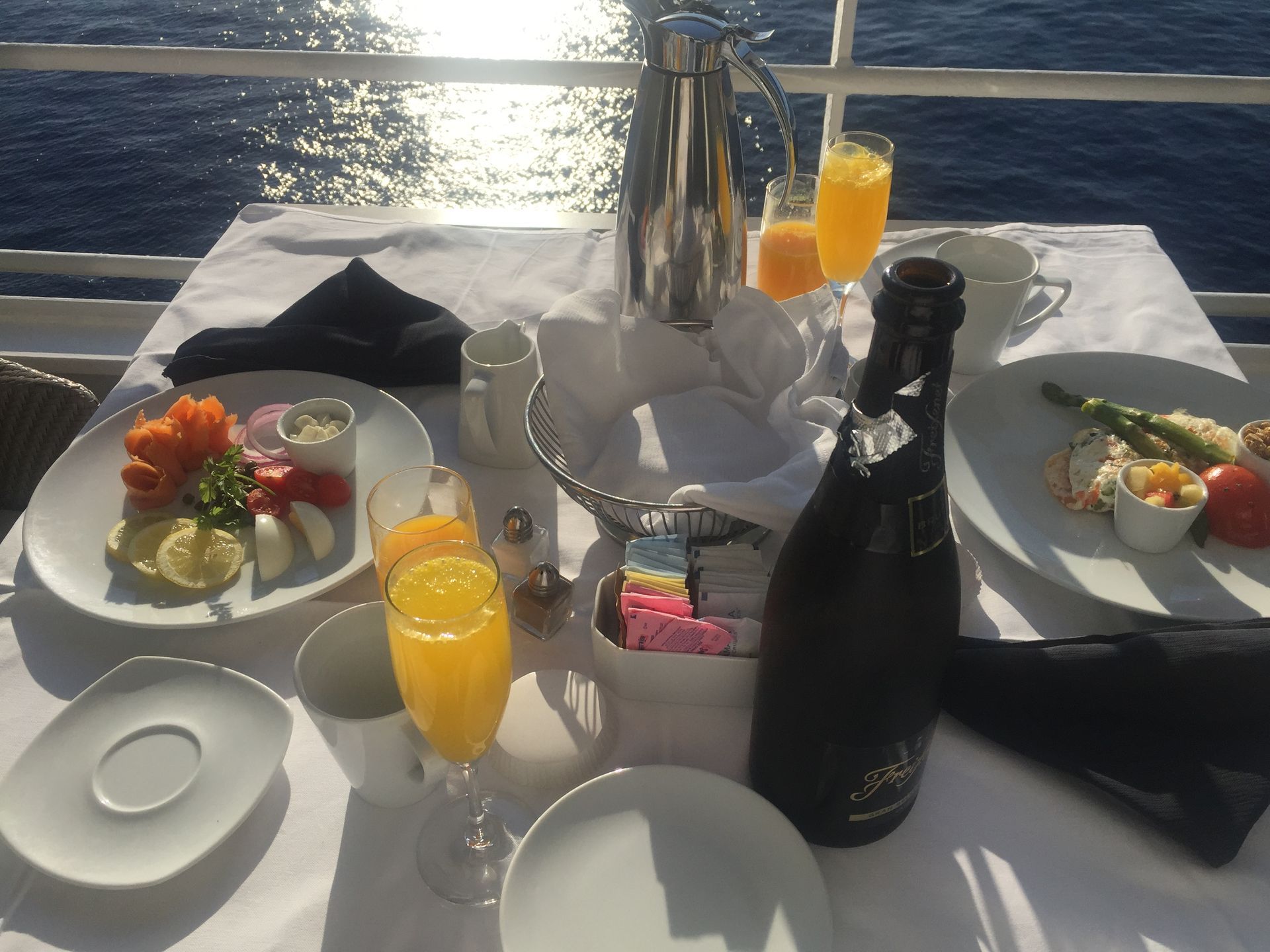 a table with plates of breakfast food and a bottle of champagne on it onbaord Azamara Quest
