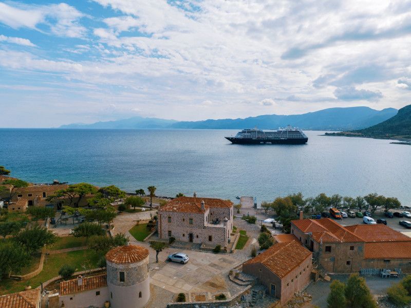 Coastal view with buildings, blue sea, and an azam cruise ship under a cloudy sky.