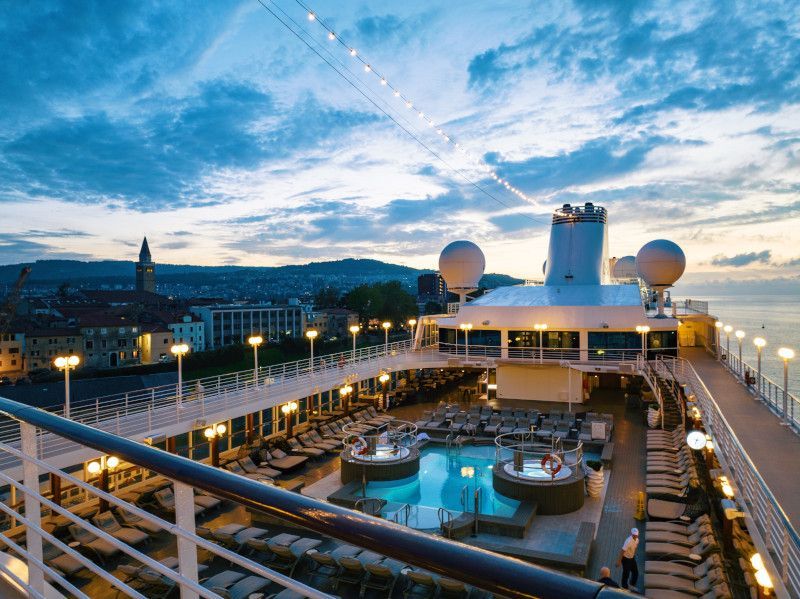 Pool Deck on Azamara Cruises Cruise ship deck with pool, overlooking city at dusk.