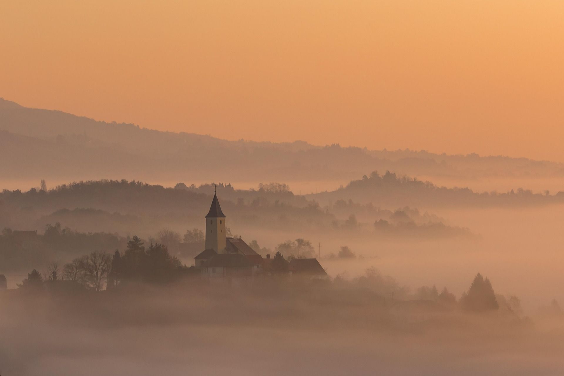 A church in the middle of a foggy valley at sunset.