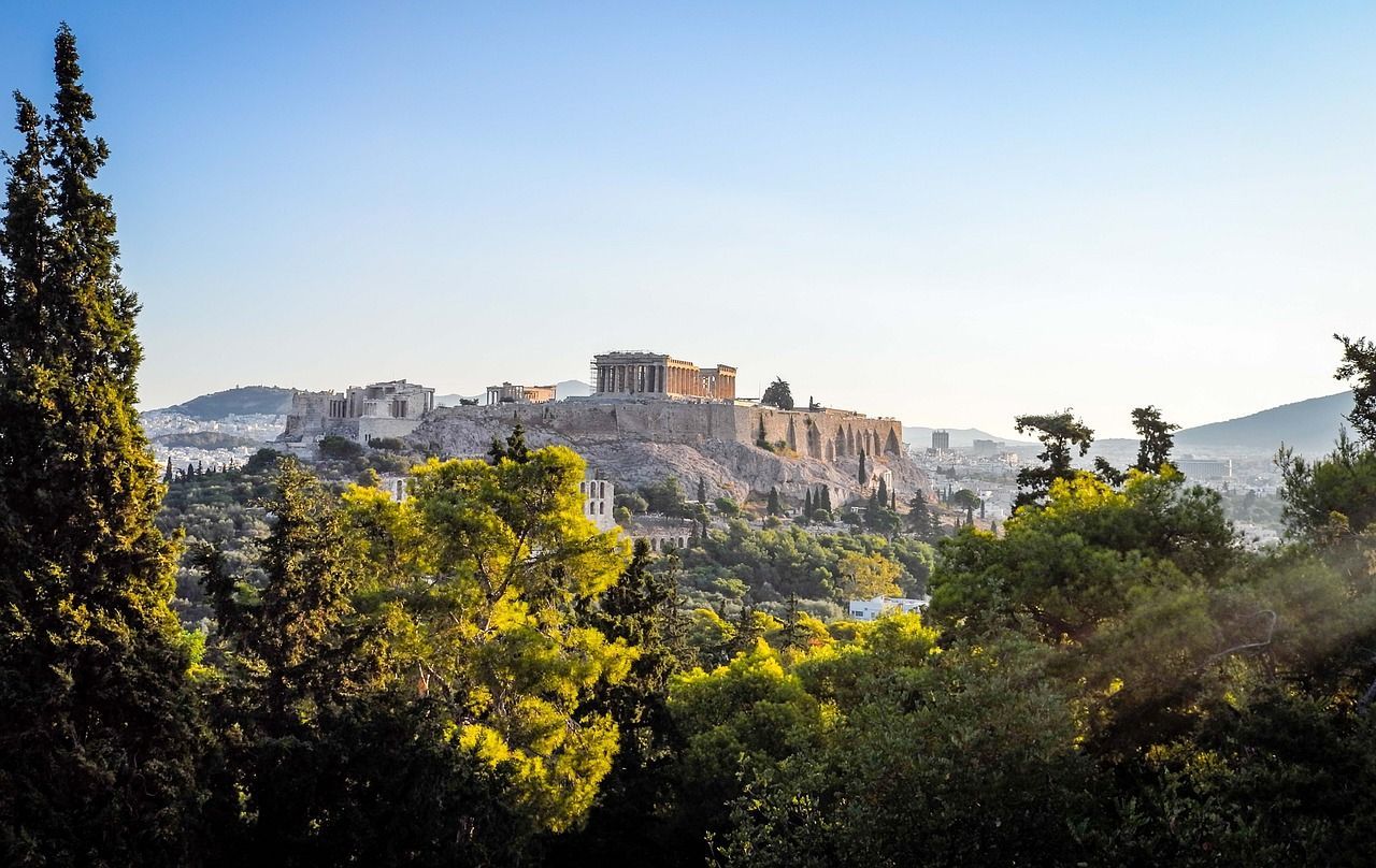 A view of the acropolis from the top of a hill surrounded by trees.