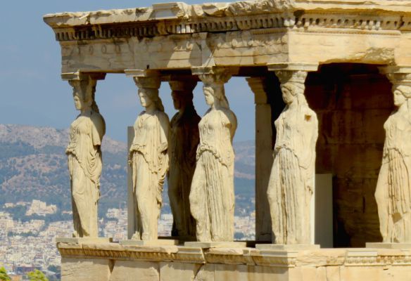 A row of statues on a building with mountains in the background in Athens
