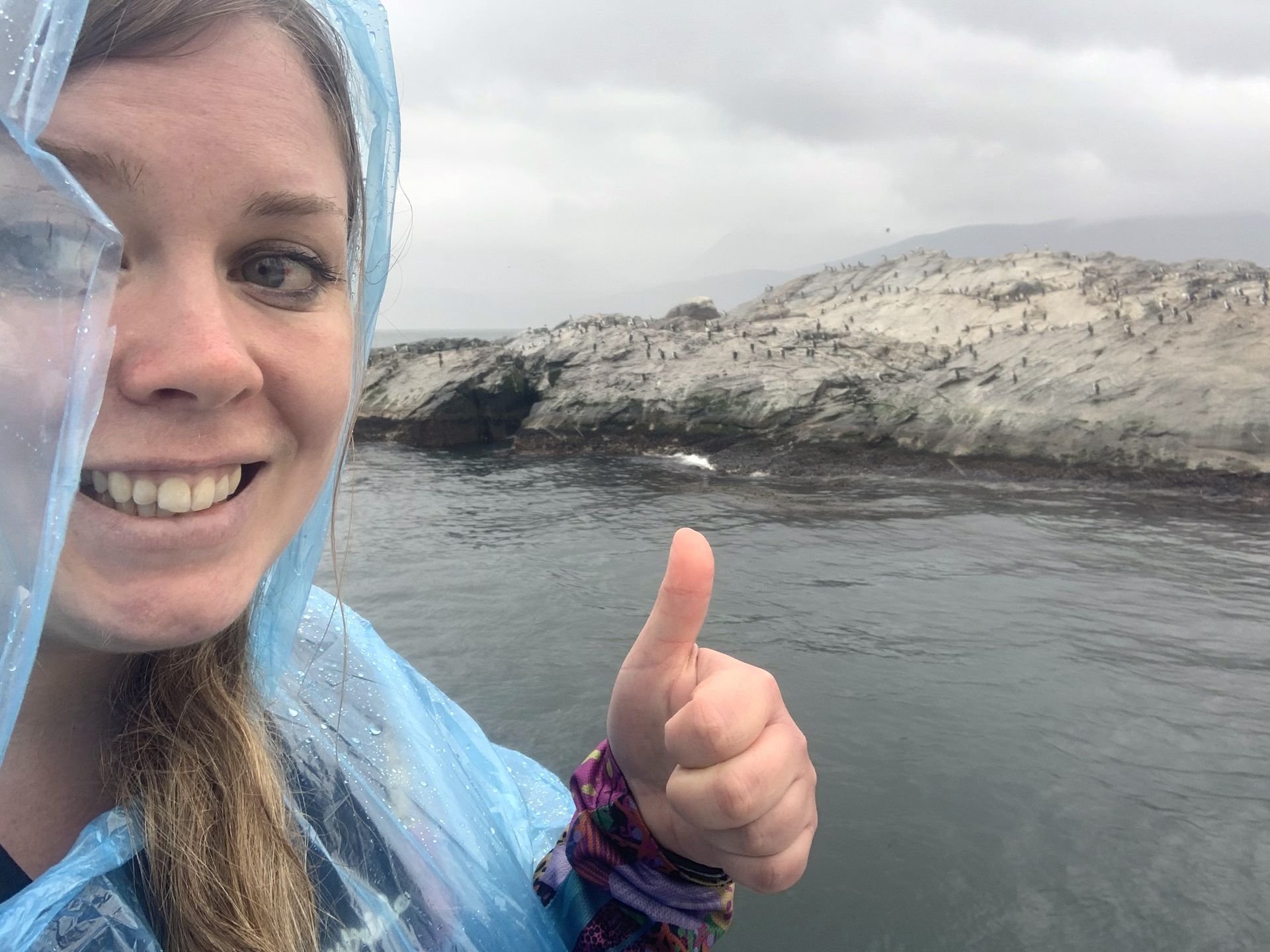 A woman in a blue raincoat is giving a thumbs up.