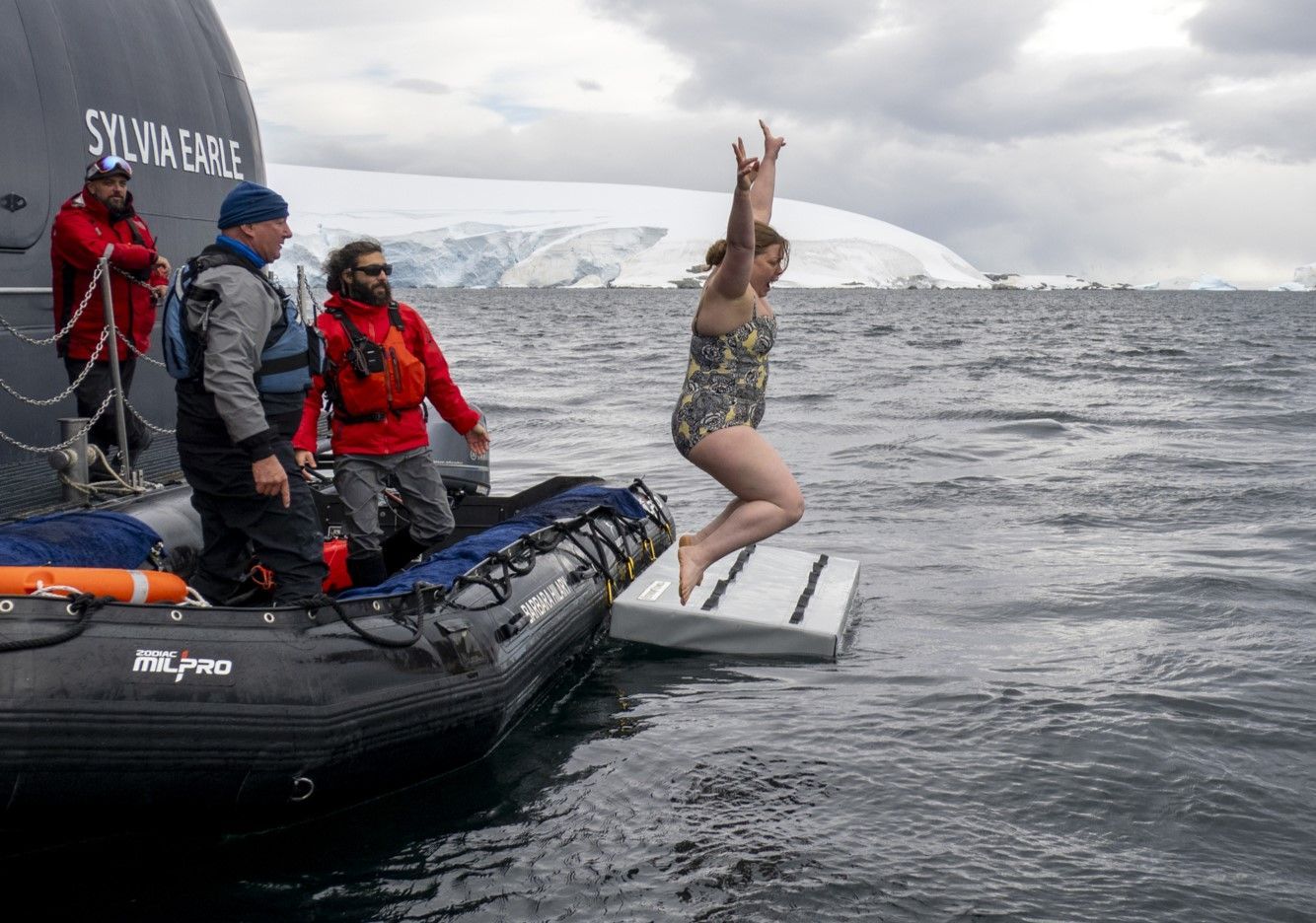 A woman is jumping out of a boat into the water in Antarctica