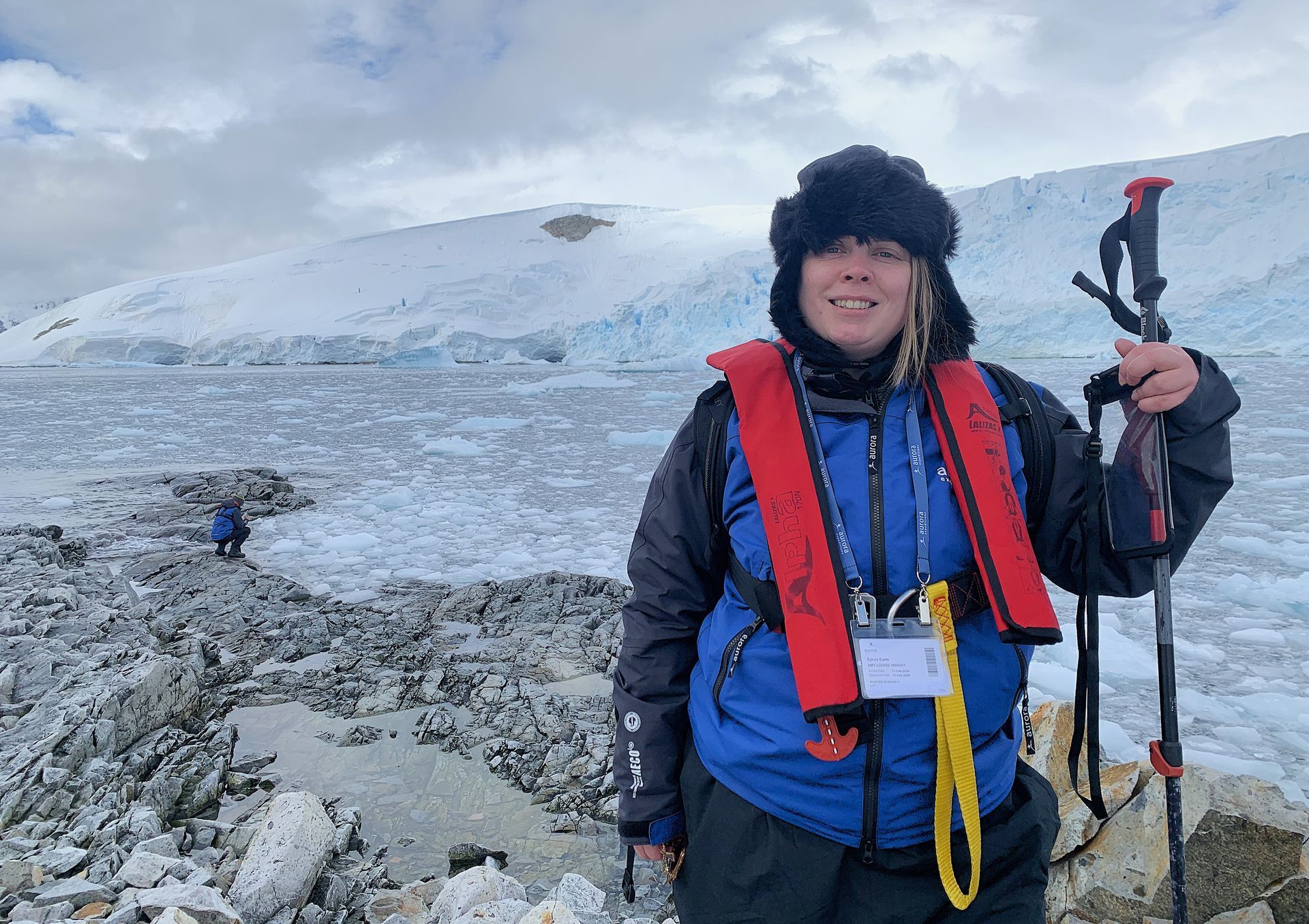 A woman wearing a life jacket is standing in front of a glacier in Antarctica