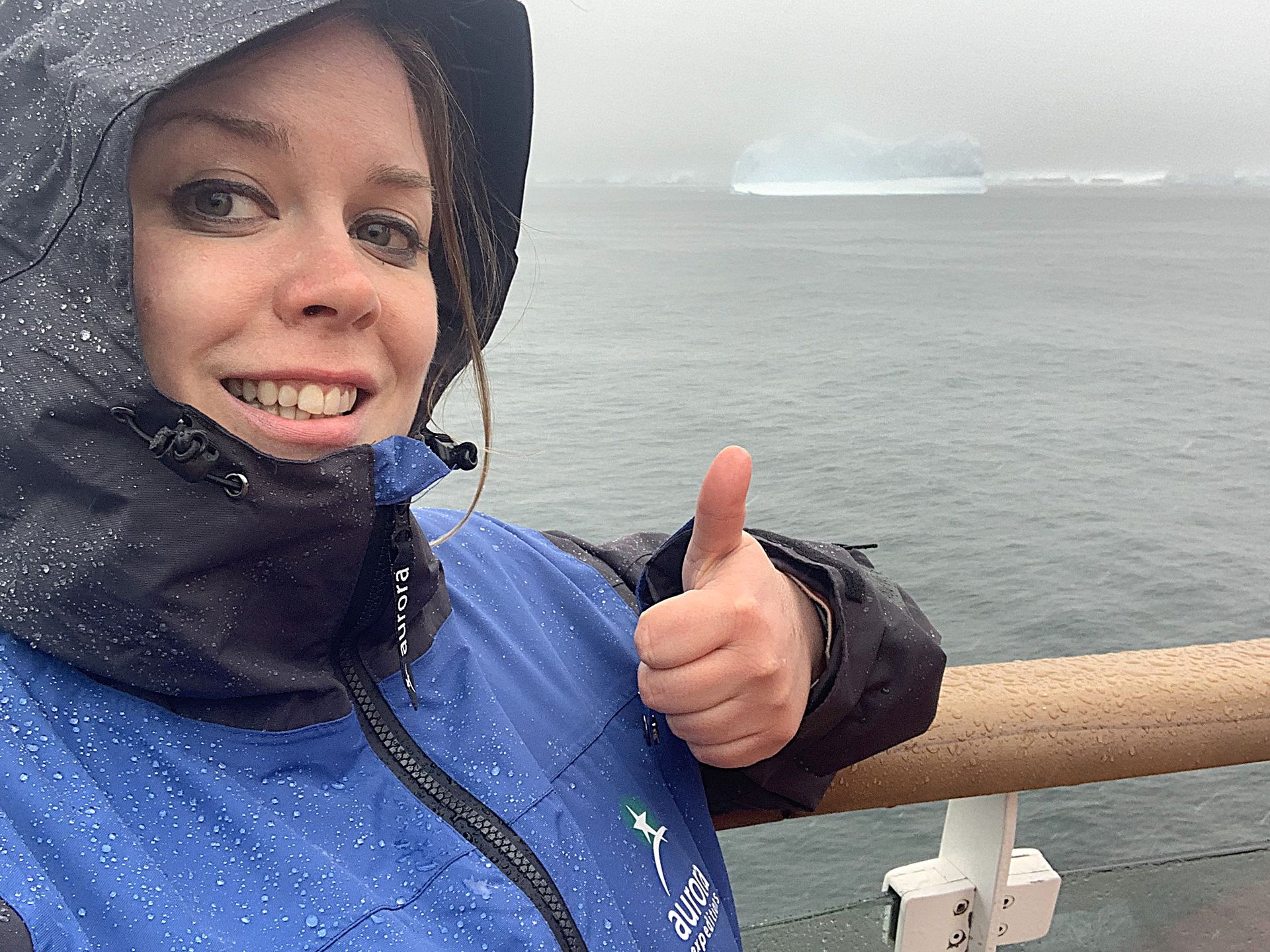 A woman in a blue jacket is giving a thumbs up in the Drake Passage