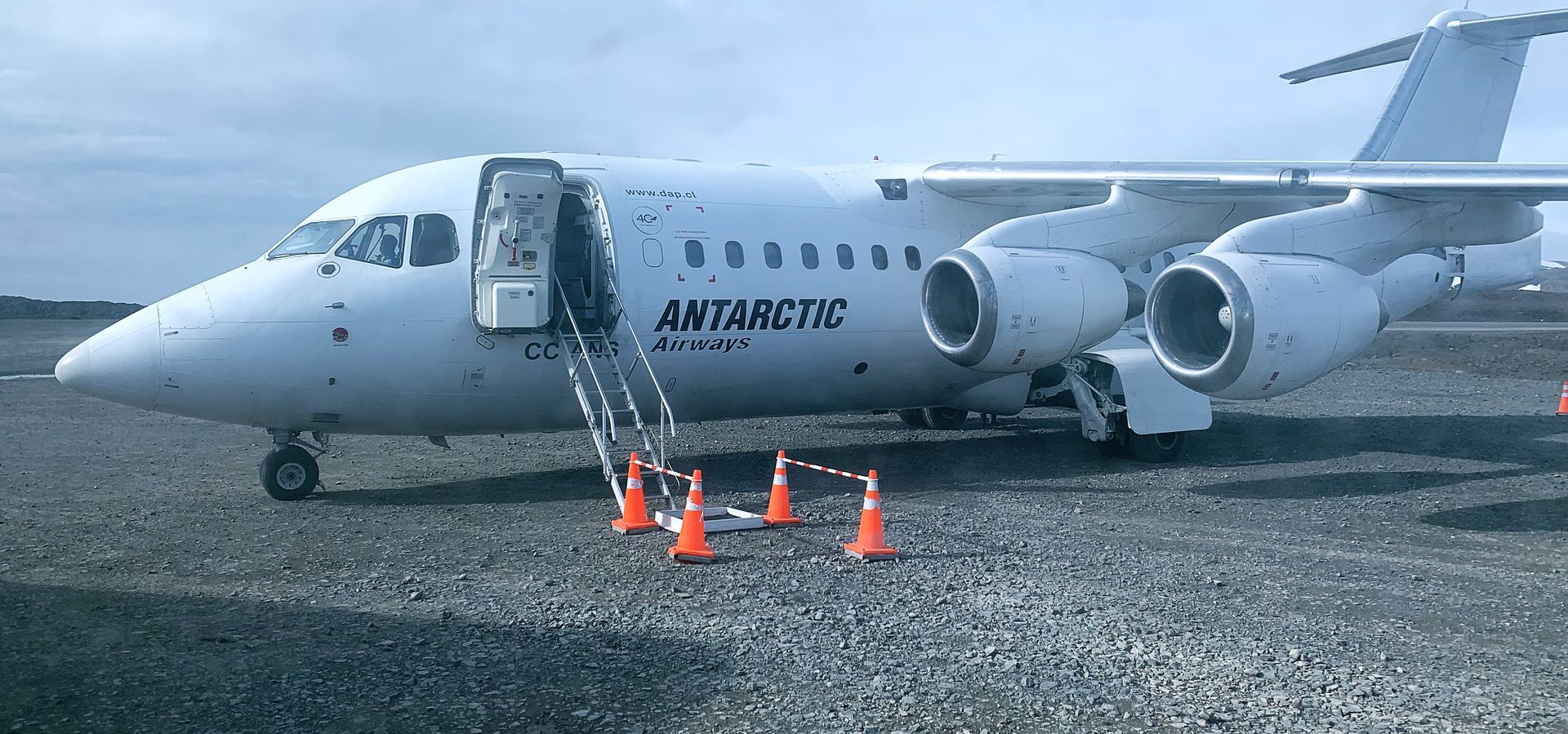 A white airplane is parked on a gravel runway with Antarctic Airways written on it