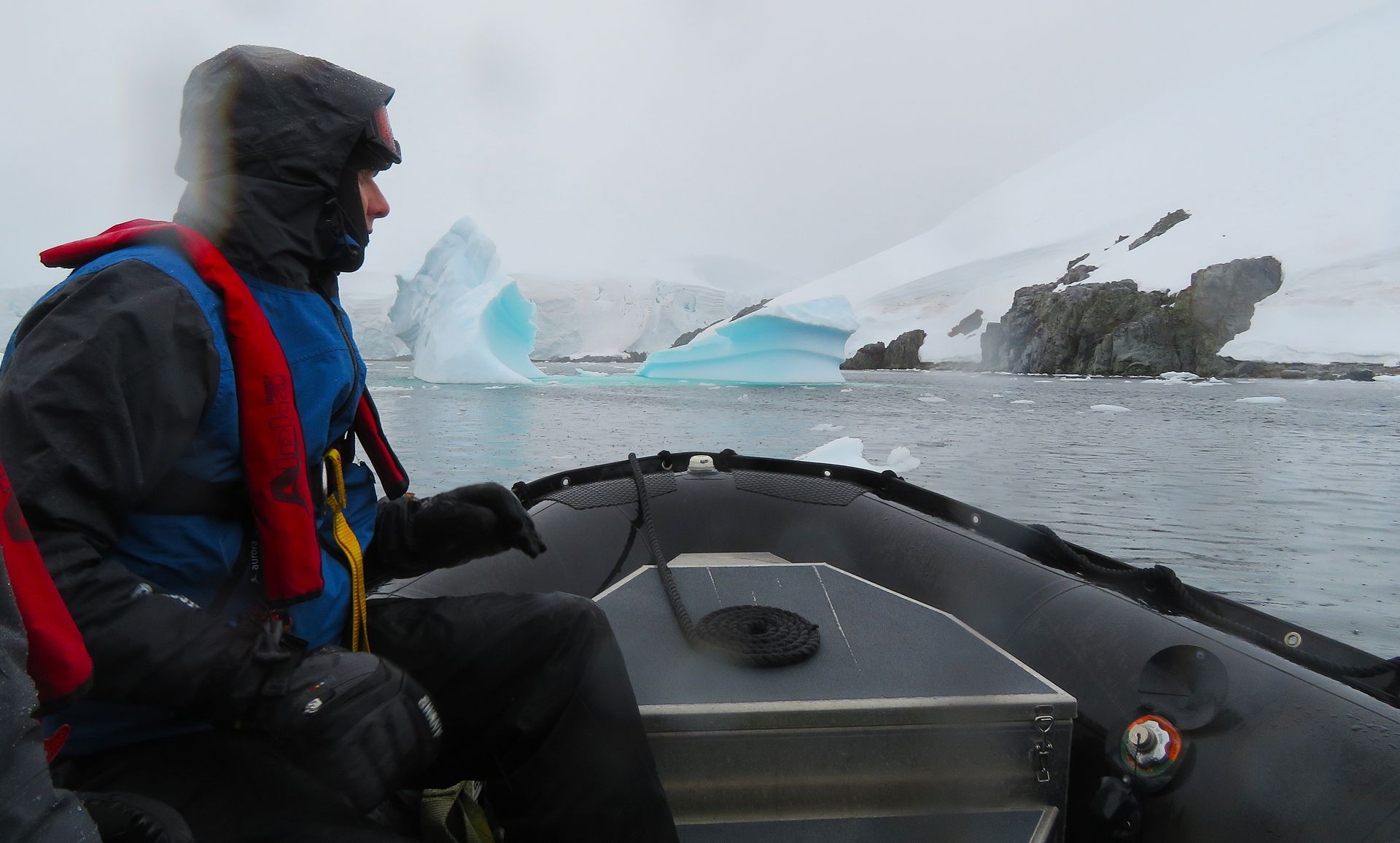 A man in a life jacket is driving a boat in the water in Antarctica