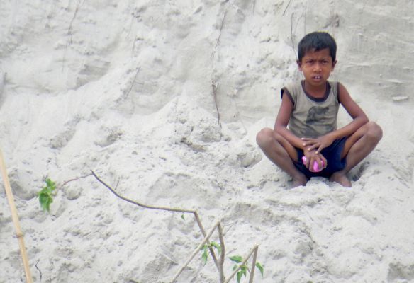 A young boy is sitting on a pile of sand