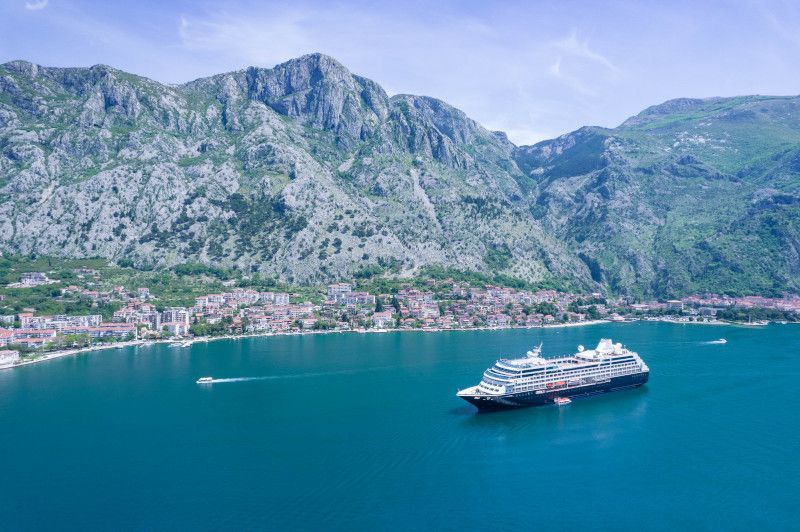 An aerial view of a cruise ship in the ocean with mountains in the background.