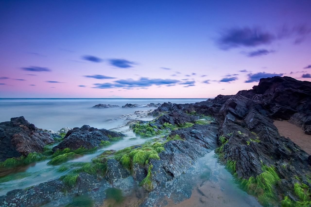 A long exposure photo of a rocky beach with a sunset in the background.