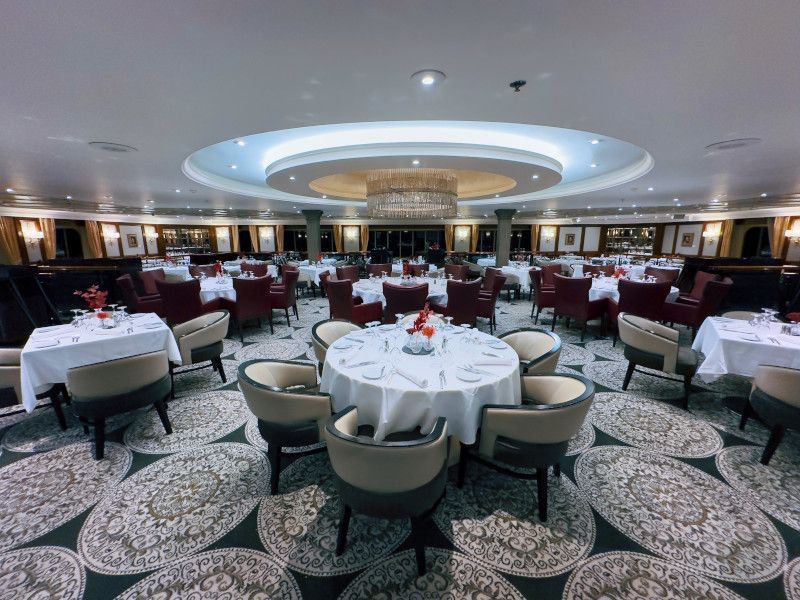 A large dining room with tables and chairs and a chandelier onboard Azamara