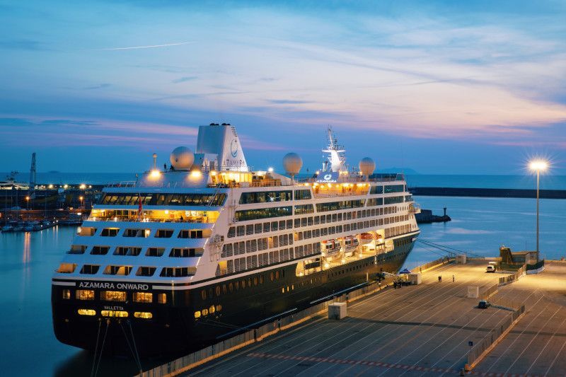 A large cruise ship is docked in a harbor at night with Azamara written on it