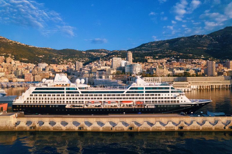 A large cruise ship is docked in a harbor with a city in the background with Azamara written on it