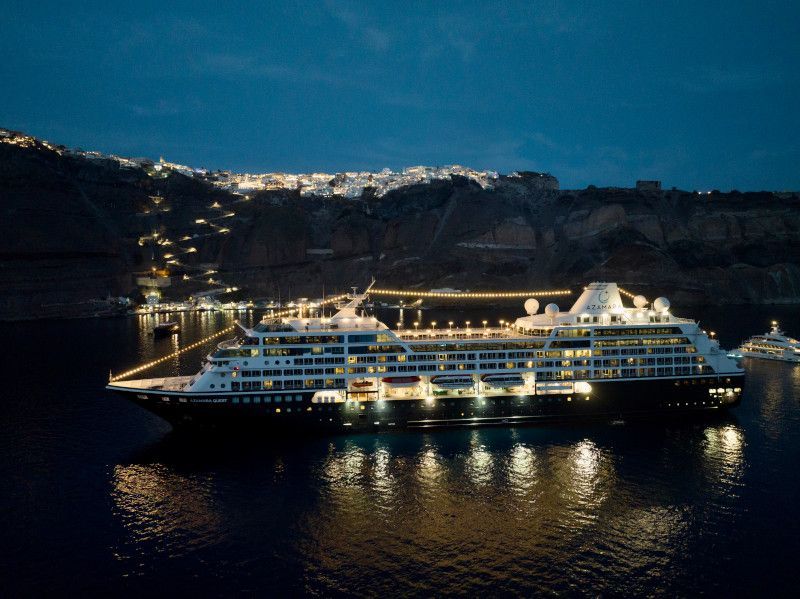 A large cruise ship is docked in a harbor at night with Azamara written on it