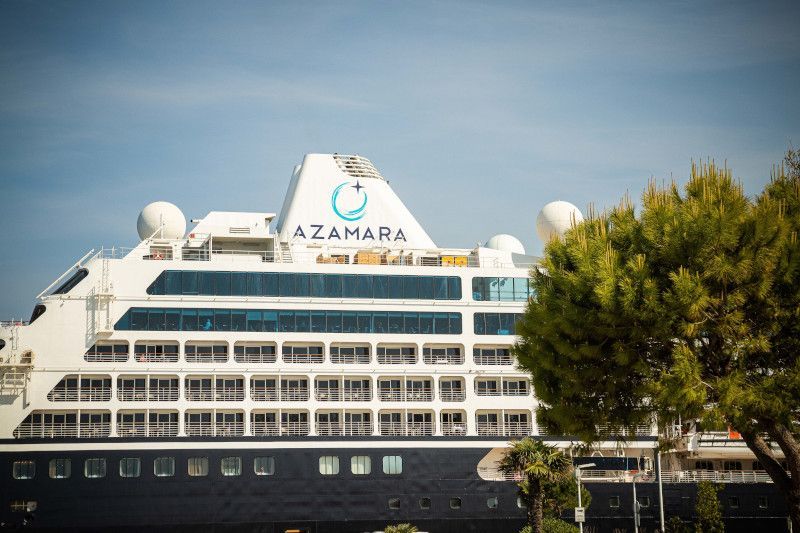 A large cruise ship is docked in a harbor next to a tree with Azamara written on funnel