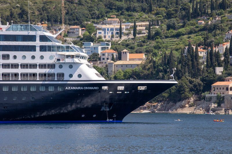 A large cruise ship is in the water near a small town with Azamara written on it