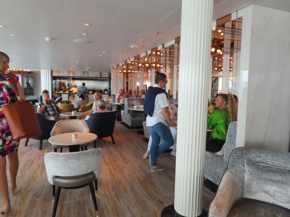 A woman is walking through a restaurant with people sitting at tables and chairs.