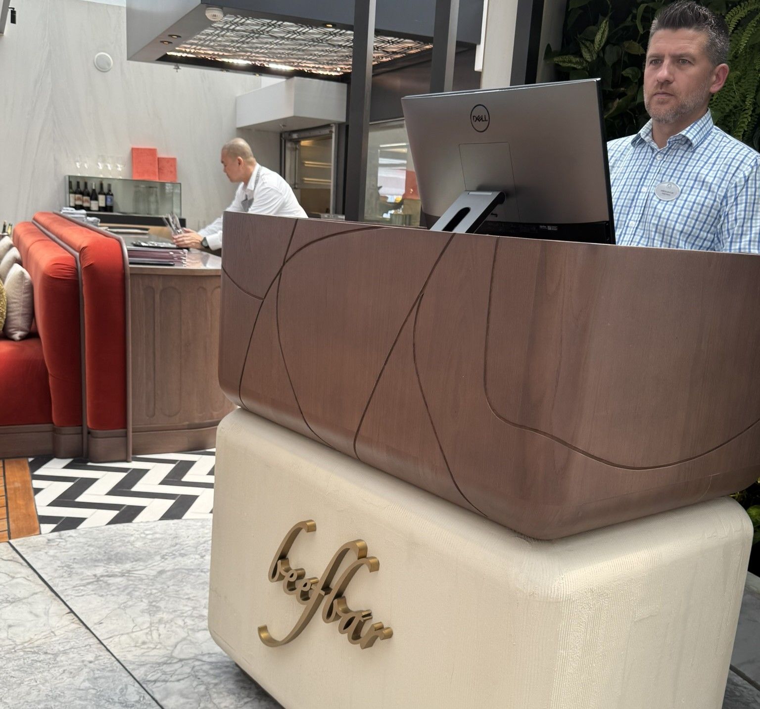 Man at restaurant reception desk, brown and cream. Another person in background.