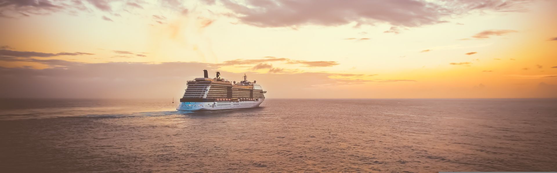 A cruise ship is floating on top of a large body of water at sunset.