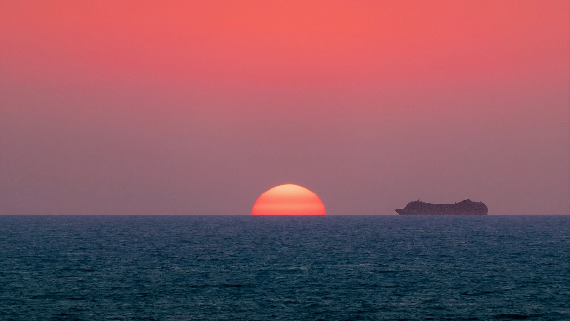 The sun is setting over the ocean with a boat in the distance.