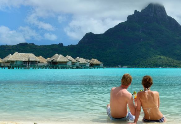 a man and a woman are sitting on the beach looking at the ocean .Top Romantic Ports - Bora Bora